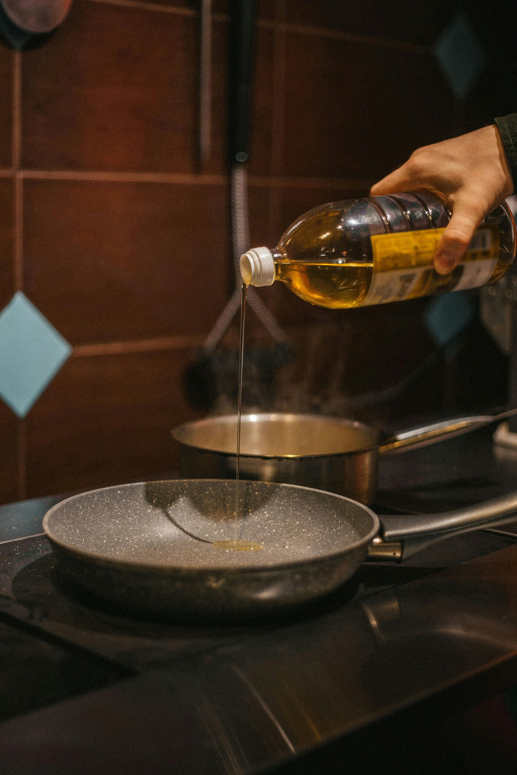 Close-up of hand pouring cooking oil into frying pan during food preparation.